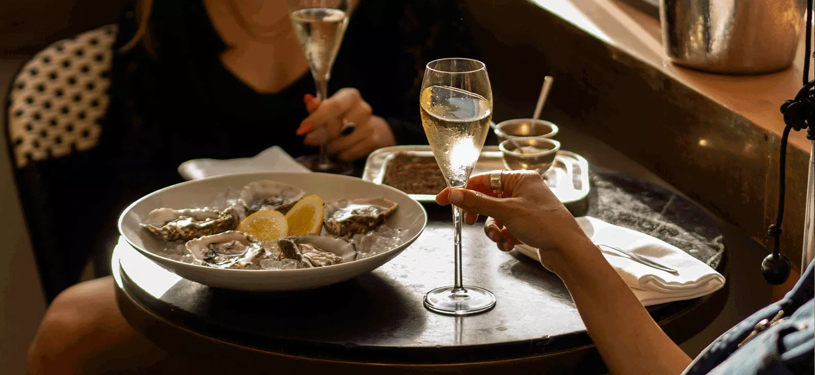 Two women enjoying a luxurious meal at Hotel Montefiore, featuring a plate of fresh oysters and glasses of champagne, in an elegant and intimate dining setting.