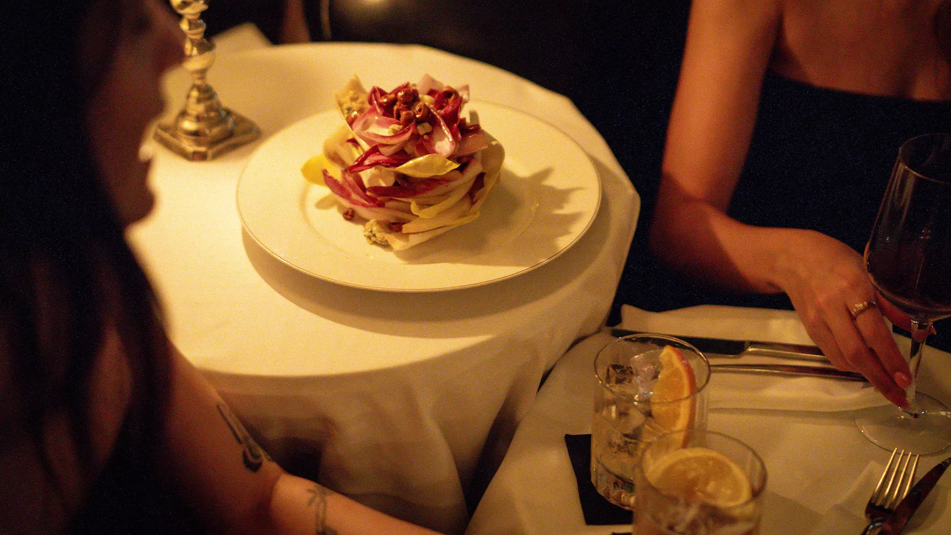 Two women dining at Hotel Montefiore in Tel Aviv, enjoying a beautifully plated dish in an intimate, luxurious setting. The ambiance is elegant with dim lighting and sophisticated decor, highlighting the restaurant's fine dining experience.